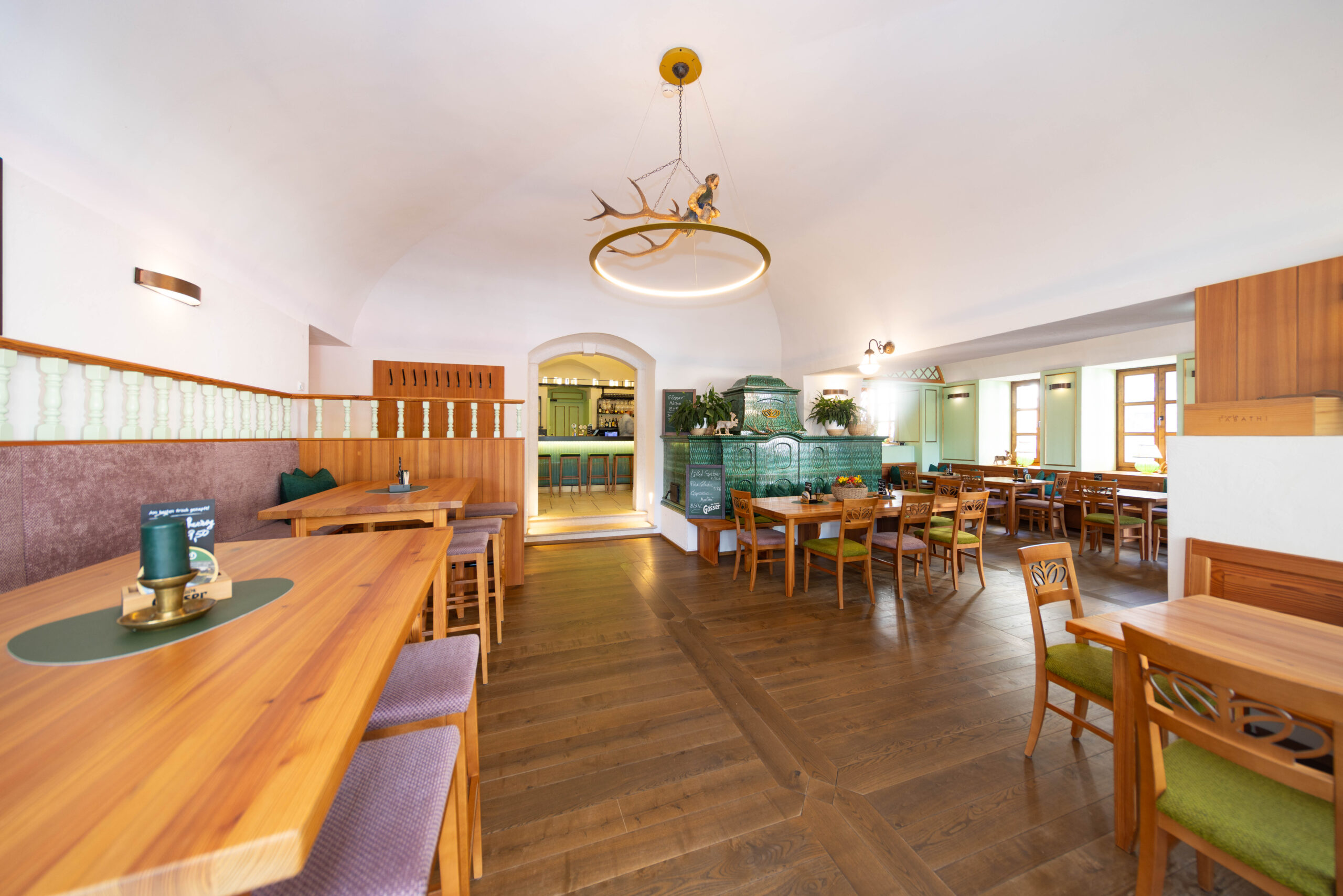 Gastraum im Wirtshaus s'JOHANN mit dem grünen Kachelofen im Hintergrund unt Tischen im Vordergrund.