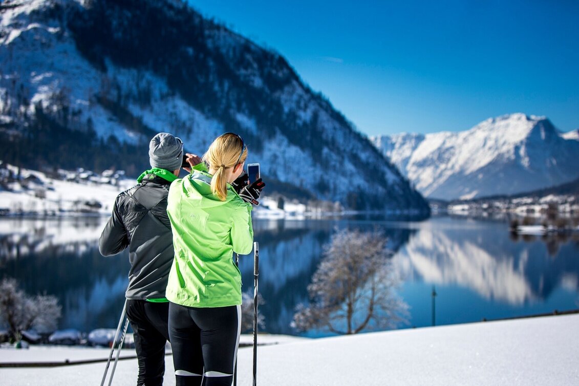 Zwei Langläufer machen ein Foto vom Altausseer See im Winter.