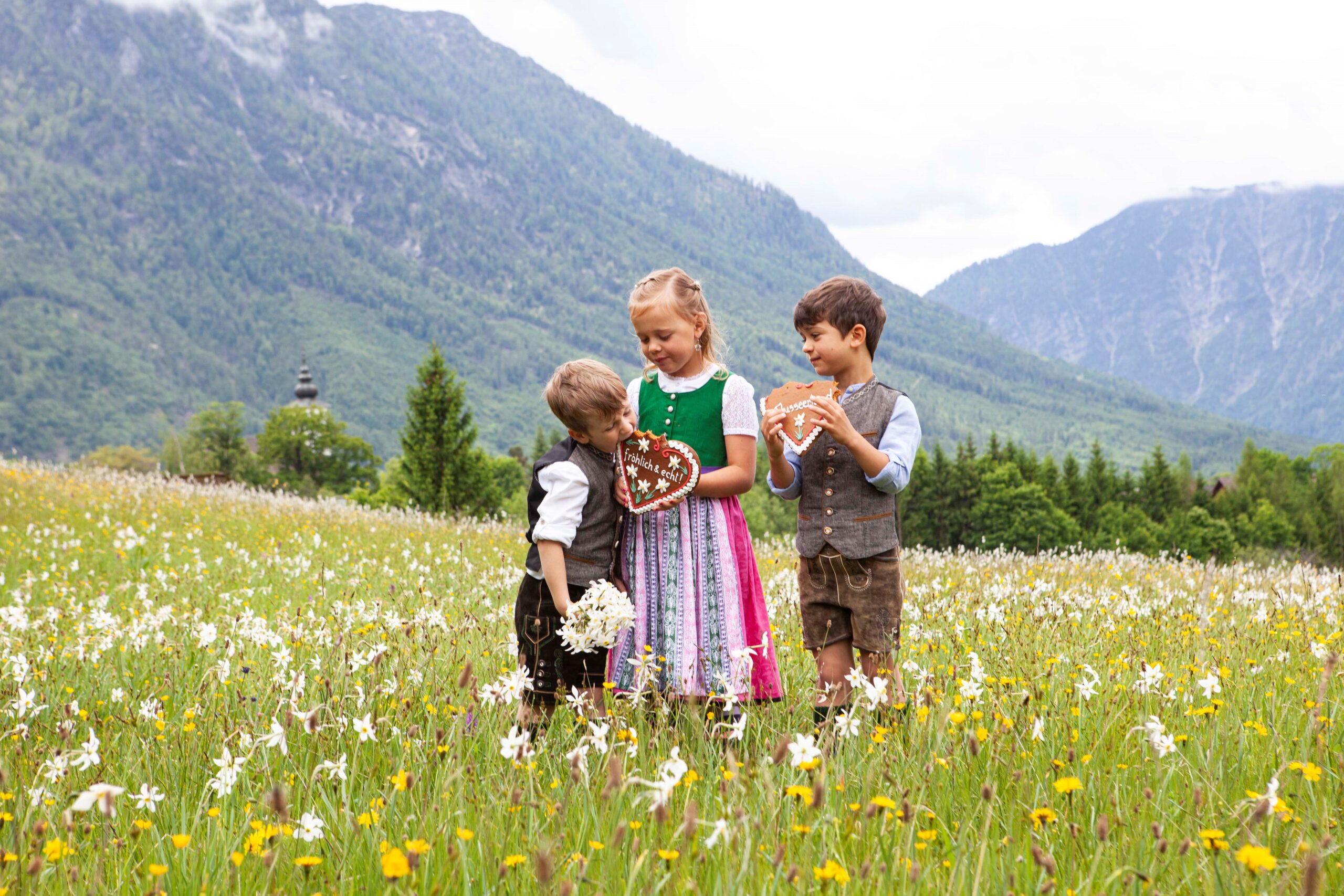 Drei Kinder mit einem Lebkuchenherz in der Wiese.