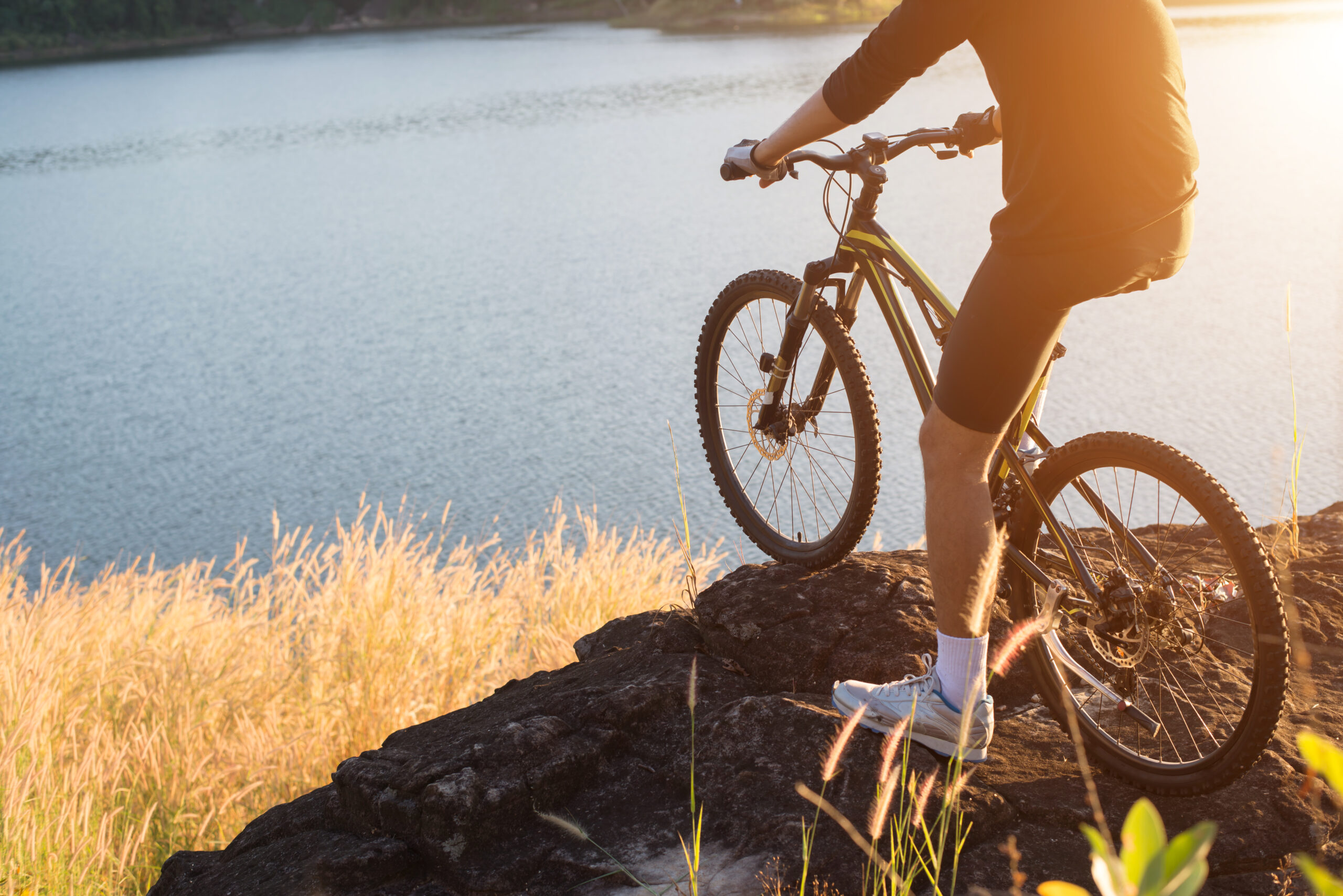 Radfahrer auf einem Felsen, schaut auf einen See hinunter.